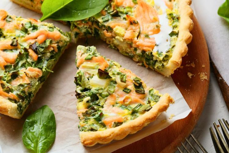 Una quiche de salmón y espinacas con un trozo cortado.