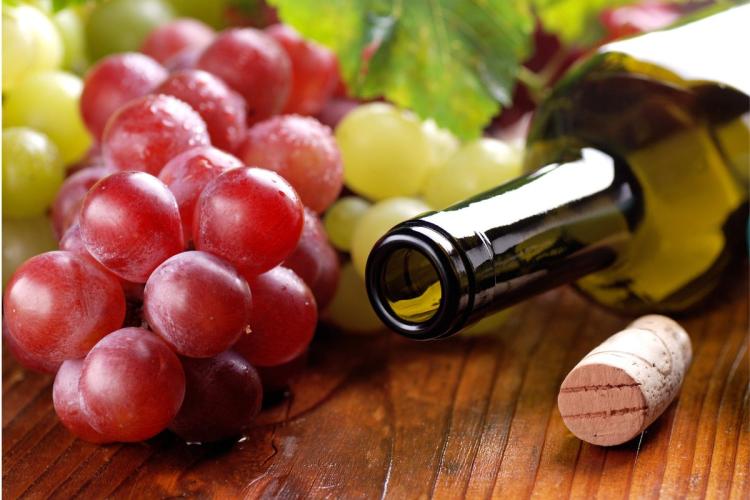 Una botella de vino abierta con el corcho a un lado y racimos de uvas al otro lado.