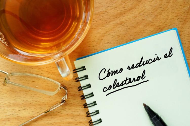 Un cuaderno con una frase, cómo reducir el colesterol, escrita al lado de una taza con una infusión.