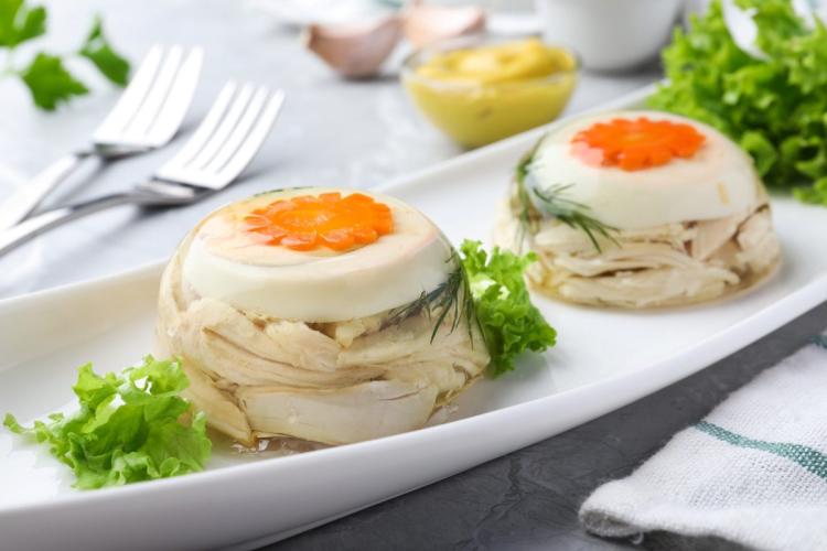 Dos áspic de ave de tamaño individual en una fuente blanca, adornados con hojas de ensalada.