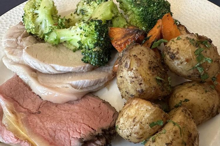 Un plato con lonchas de dos tipos de carne asada, cerdo y vacuno, servidas con verduras y patatas.
