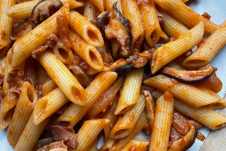 Detalle de pasta corta, plumas, con setas y jamón serrano.