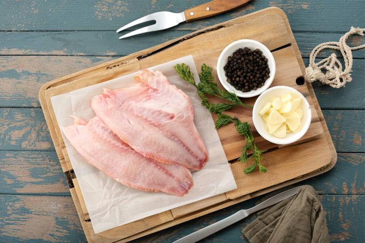 Filetes de tilapia crudos junto con los condimentos que se van a utilizar en cocinarlos.
