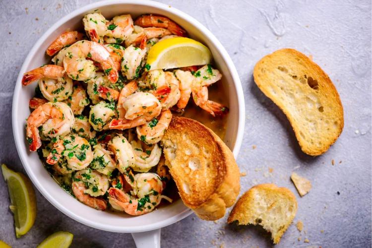 Gambas con salsa de mantequilla, ajo y limón en cacito de loza, acompañadas con rebanadas de pan tostado.