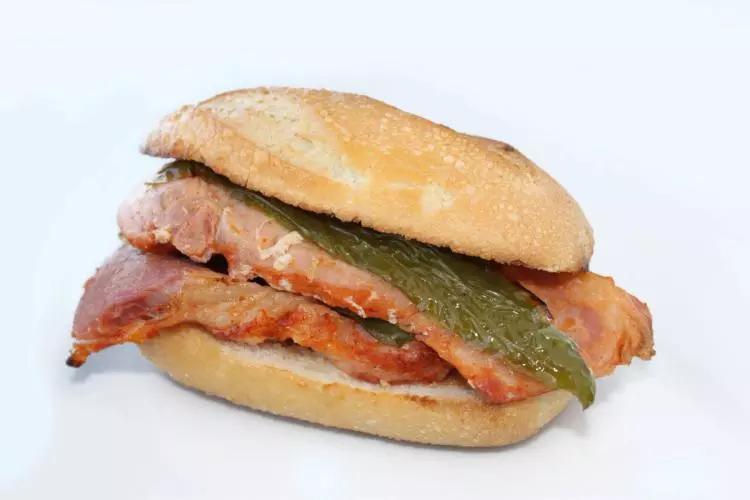 Un montadito de lomo en panecillo individual, con dos filetes de lomo de cerdo fritos y una tira de pimiento verde.