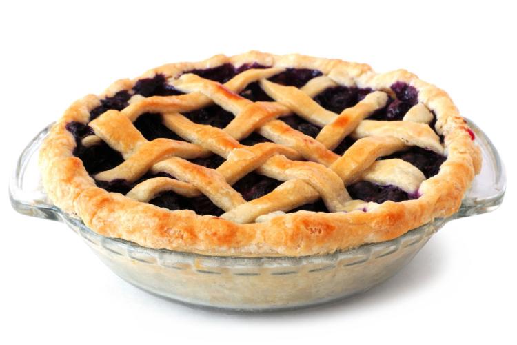 Tarta americana de arándanos azules con cubierta de rejilla de masa dorada, horneada en un molde de vidrio transparente sobre fondo blanco.