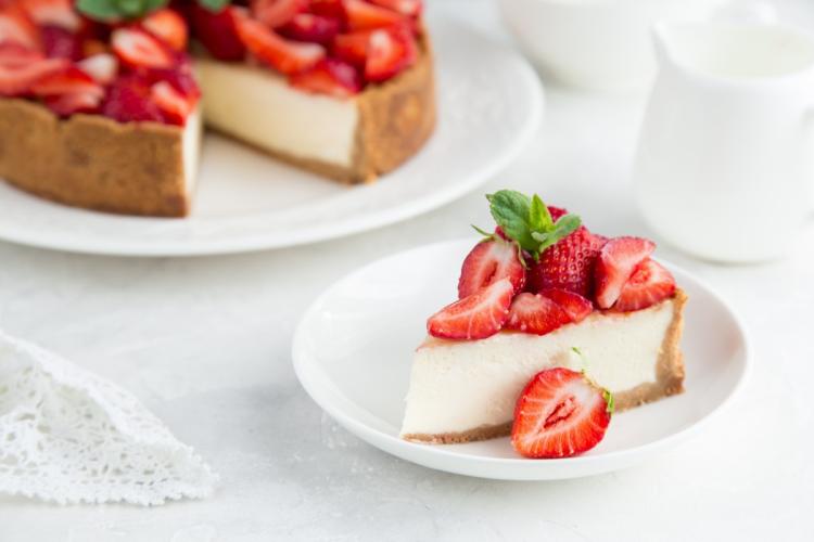 Porción de tarta de queso cubierta con fresas frescas y hojas de menta, servida en un plato blanco.