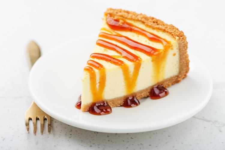 Porción de tarta de queso con salsa de caramelo sobre un plato blanco, acompañada de un tenedor dorado.
