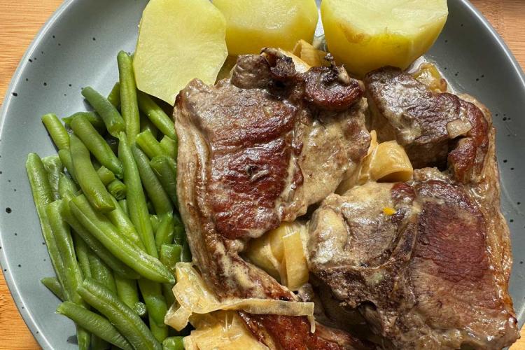 Chuletas de cordero doradas con salsa cremosa de puerro, servidas en un plato con judías verdes y patatas cocidas.