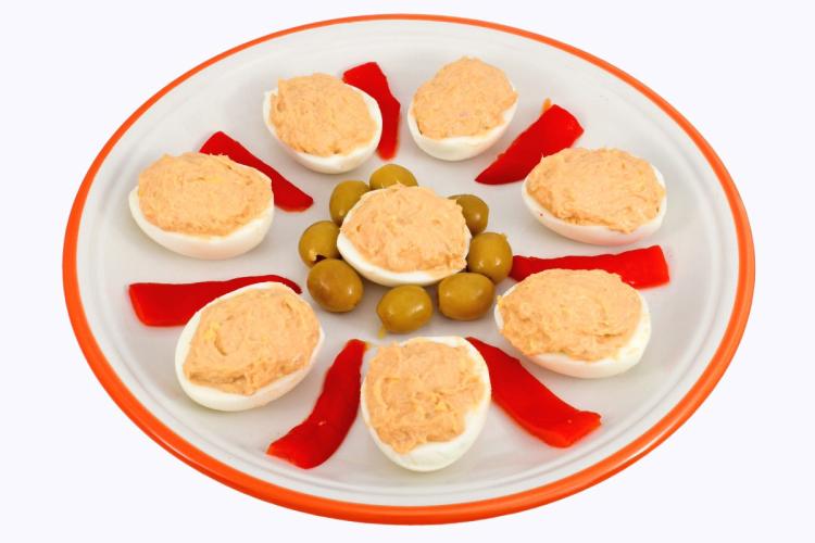 Huevos rellenos con yema, atún y salsa de tomate, servidos con aceitunas verdes y tiras de pimiento rojo.