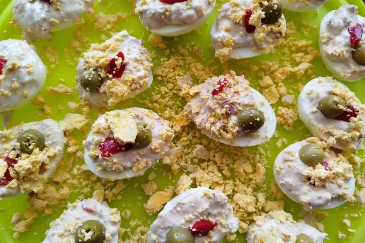 Huevos rellenos con queso crema, aceituna verde y trocitos de pimiento, decorados con yema de huevo duro desmenuzada.
