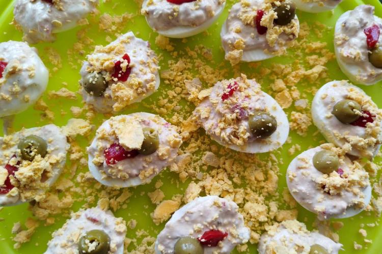 Huevos rellenos con queso crema, aceituna verde y trocitos de pimiento, decorados con yema de huevo duro desmenuzada.