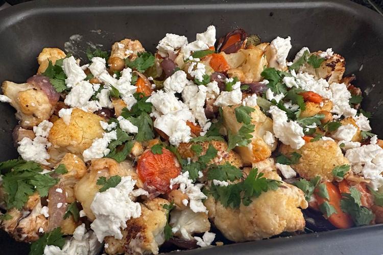 Bandeja de horno con coliflor asada, zanahoria, garbanzos y cebolla, cubierta con queso feta desmenuzado y cilantro fresco.
