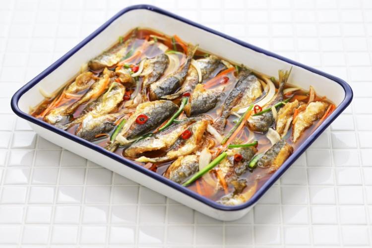 Filetes de caballa en escabeche con tiras de zanahoria, cebolla, cebolleta y rodajas de guindilla, en una fuente blanca de borde azul.