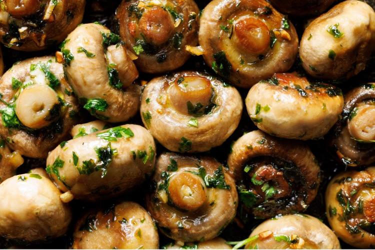 Champiñones enteros asados al horno, brillantes, con ajo picado y perejil fresco.