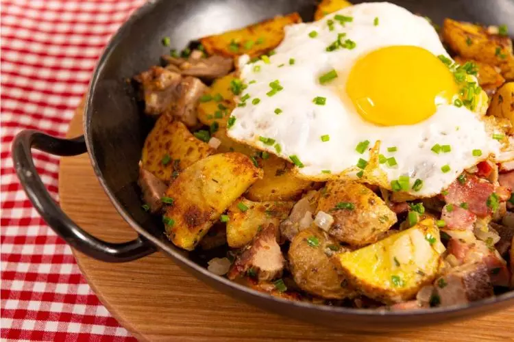 Gröstl tirolés en una sartén de hierro: patatas en rodajas doradas con tiras de carne asada y cebolla, coronado con un huevo frito.