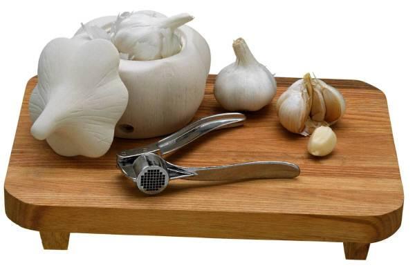 Cabezas de ajo, dientes de ajo y prensa para ajos sobre una tabla de madera.