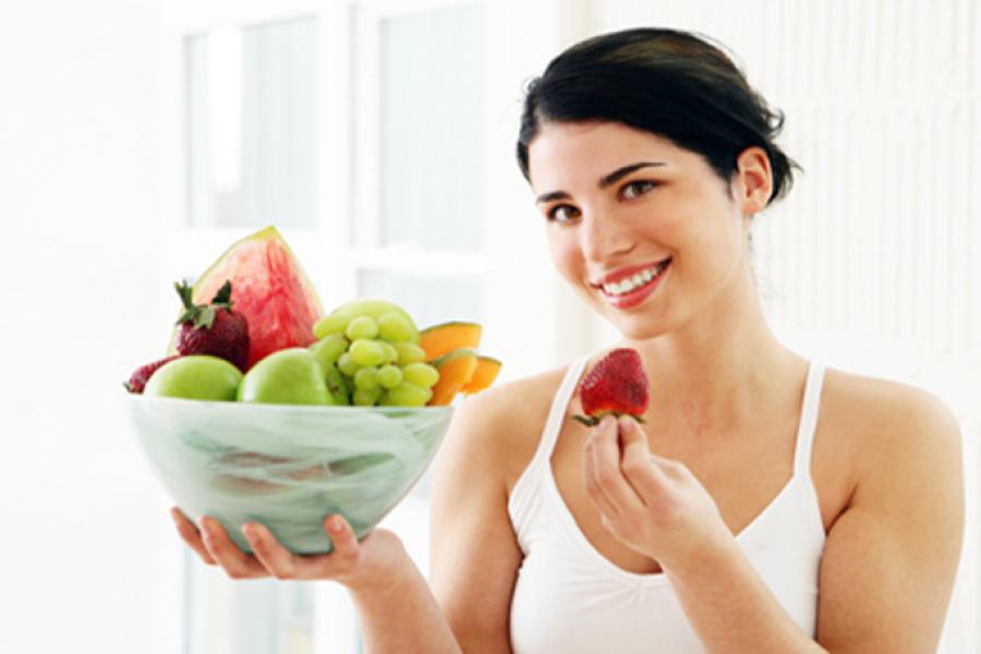 Mujer sosteniendo un frutero lleno de fruta variada.