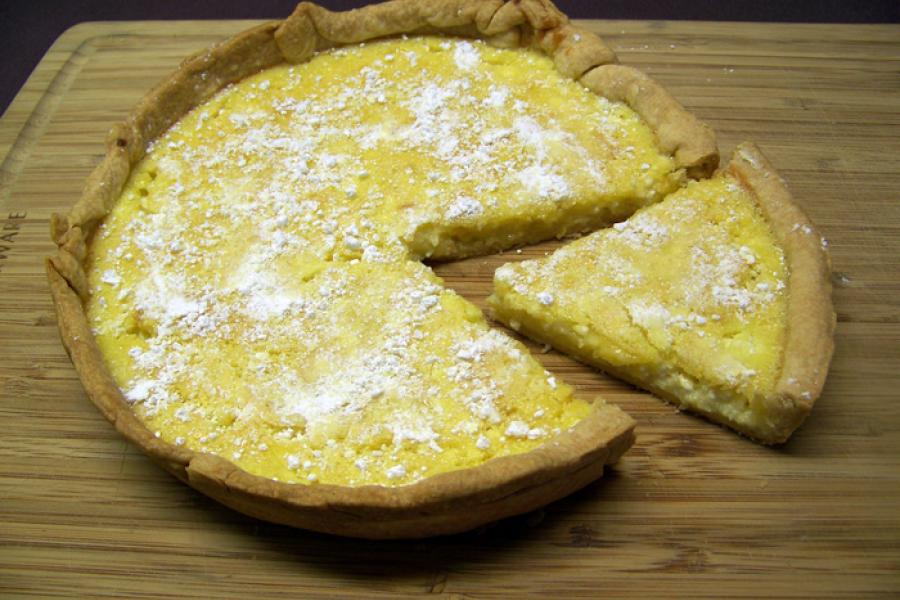 Una tarta de requesón y crema de limón sobre una tabla de madera con un trozo cortado.