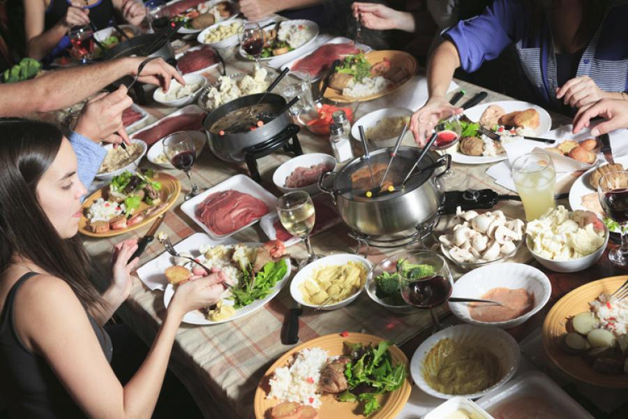Un grupo de amigos compartiendo fondue sentados alrededor de una mesa.
