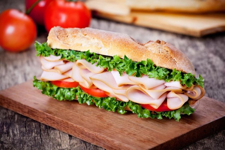 Bocadillo de fiambre de pavo con ensalada en barra de pan con mantequilla.