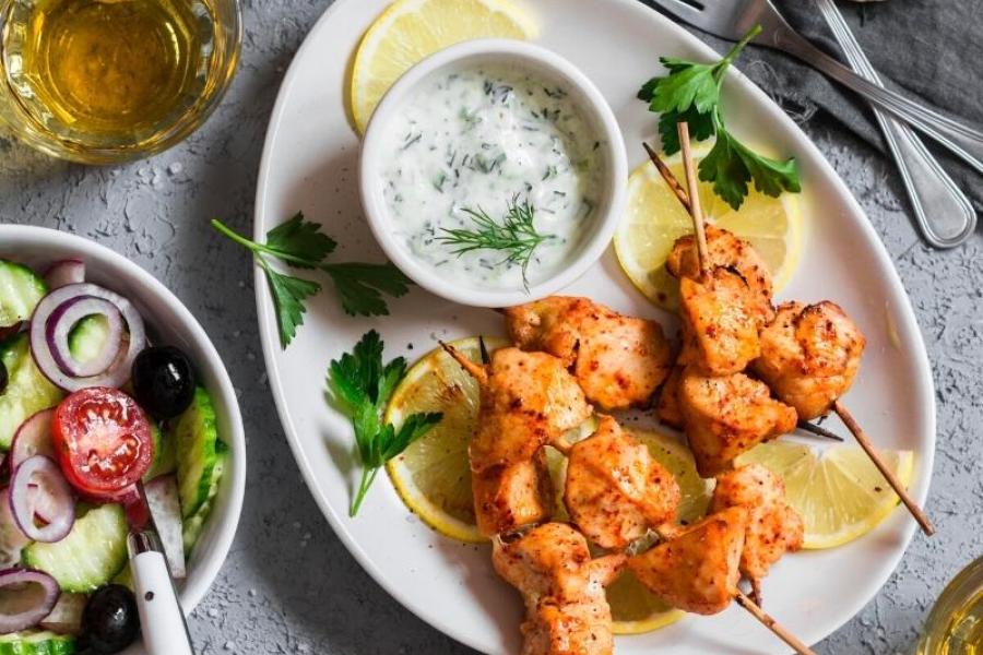 Pinchos de pollo al yogur estilo griego con tzatziki, ensalada y pan pita.