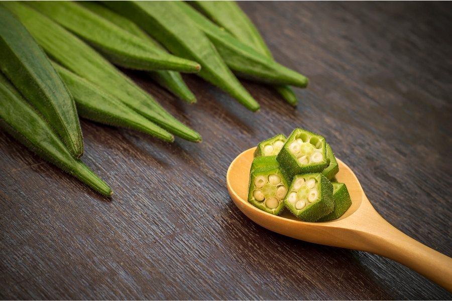 Ocra fresca, puntas de vainas enteras y unos trozos en una cuchara de madera.