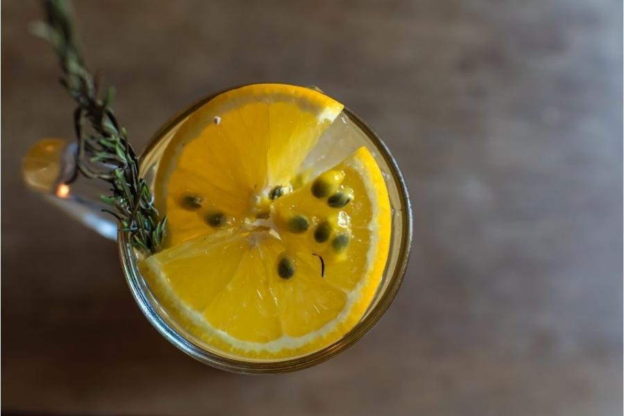 Un vaso con pasión de naranja decorada con rodaja de naranja, semillas de fruta de la pasión y una ramita de romero.