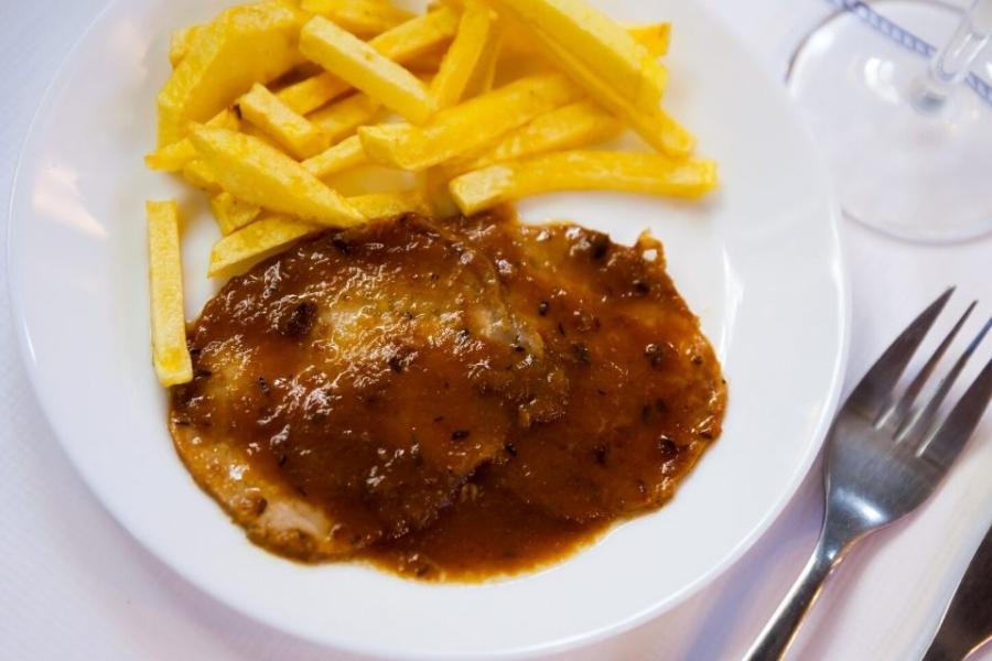 Un plato con carne mechada y su salsa acompañadas con patatas fritas.