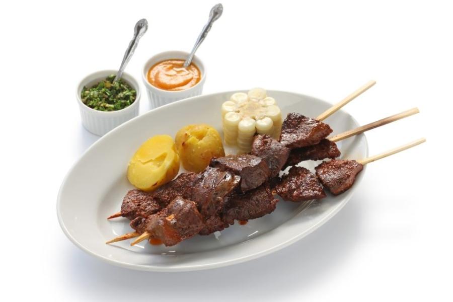 Anticuchos de corazón con patata cocida, choclo y salsas.