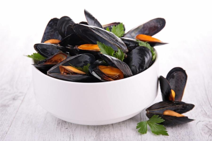Un cuenco blanco con mejillones ya cocidos decorados con perejil.
