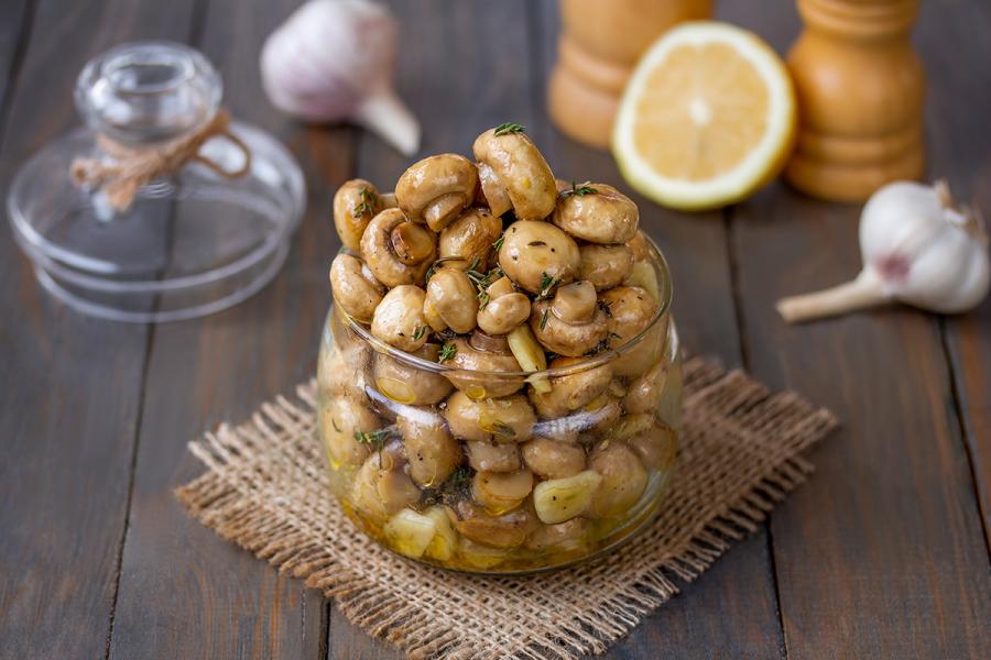 Un tarro con champiñones a la griega rodeado de algunos de los ingredientes.