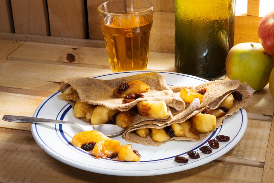 Crêpes de manzana junto a un vaso y una botella de sidra.