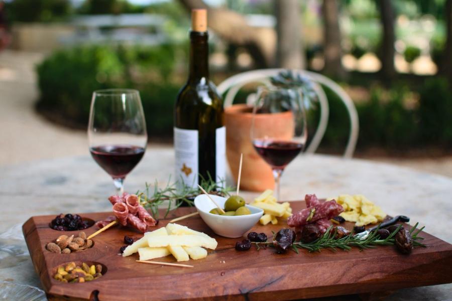 Un aperitivo con frutos secos, aceitunas, embutidos y queso acompañados de vino tinto.