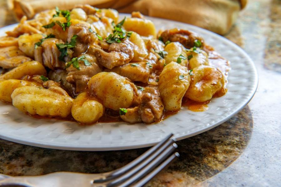 Plato de ñoquis cremosos mezclados con pollo al pimentón, servido en un plato blanco sobre una encimera de piedra.