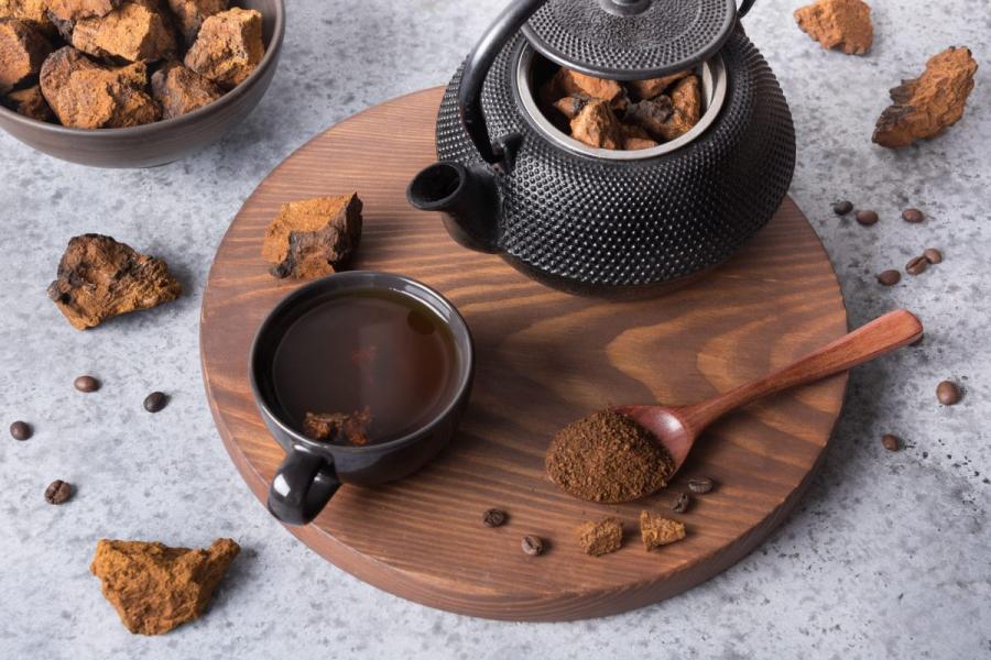 Una taza de té de hongo chaga con tetera, trozos de chaga secos y polvo sobre una tabla de madera.