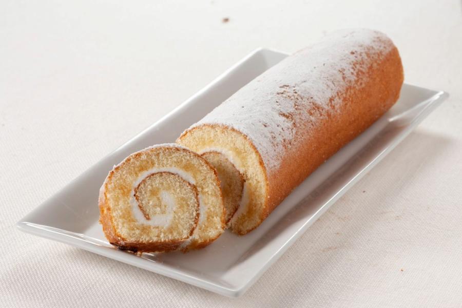 Un brazo de gitano relleno de nata, y decorado con azúcar glas, colocado sobre una fuente rectangular de loza blanca.