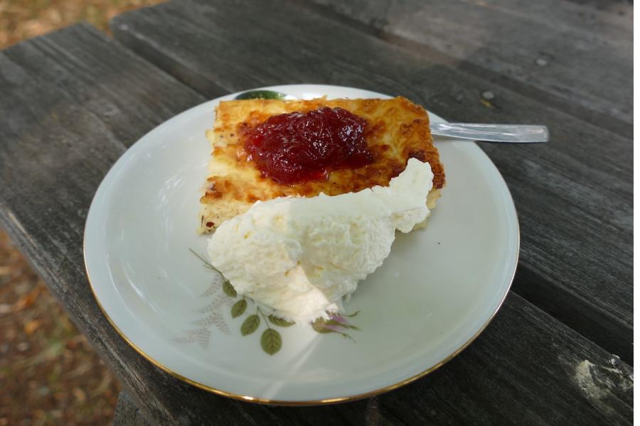 Un trozo de pastel de queso sueco, ostkaka, servido con mermelada de frutos rojos y nata montada.