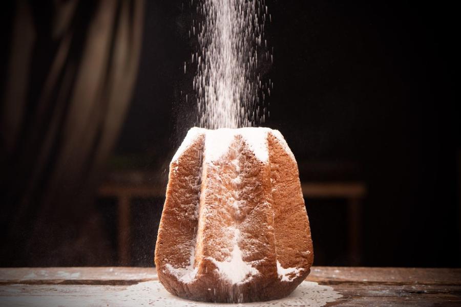 Un pandoro veronés ya hecho y enfriado a temperatura ambiente, espolvoreando azúcar glas antes de servir.