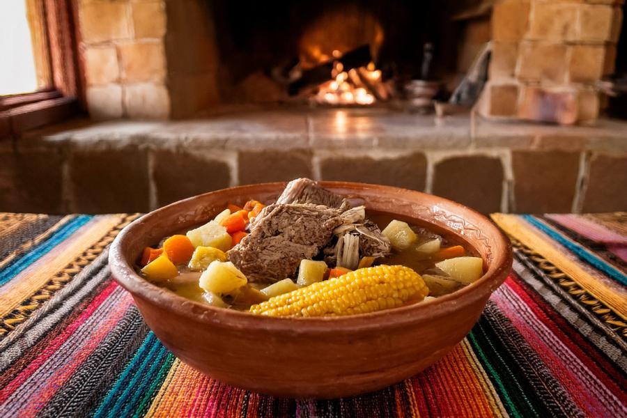 Un cuenco con picana boliviana sobre una tela típicamente andina. El fondo es una cocina rústica boliviana.