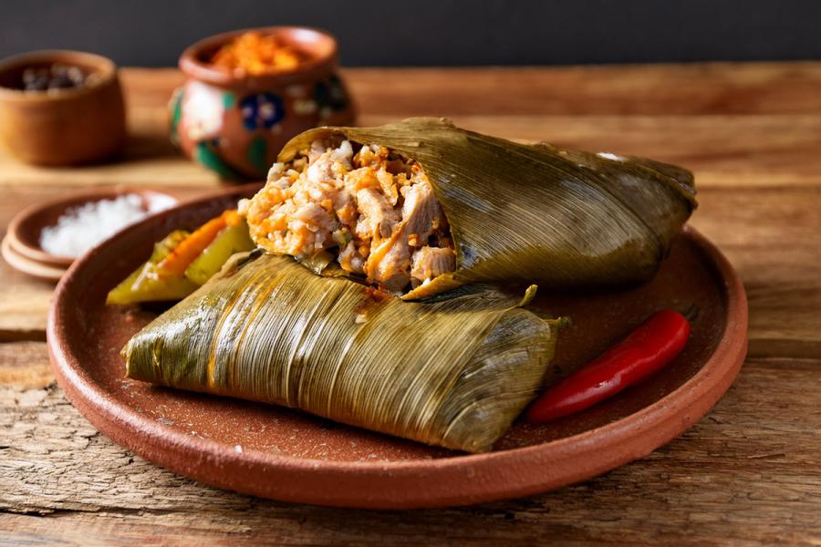 Piltes mexicanos de pollo sobre un plato de barro. Uno de ellos esta abierto, mostrando el relleno.