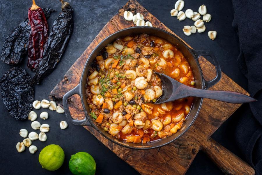 Un cuenco de pozole rojo rodeado de algunos de los ingredientes que se usan para hacerlo.