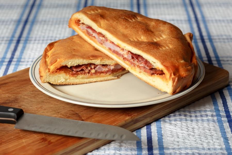 Hornazo cortado por la mitad con relleno de embutido, sobre plato y tabla de madera.