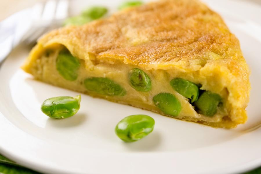 Porción de tortilla española con habas tiernas en un plato blanco.