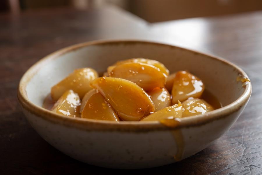 Dientes de ajo caramelizados cubiertos con almíbar dorado en un bol de cerámica sobre una mesa de madera.