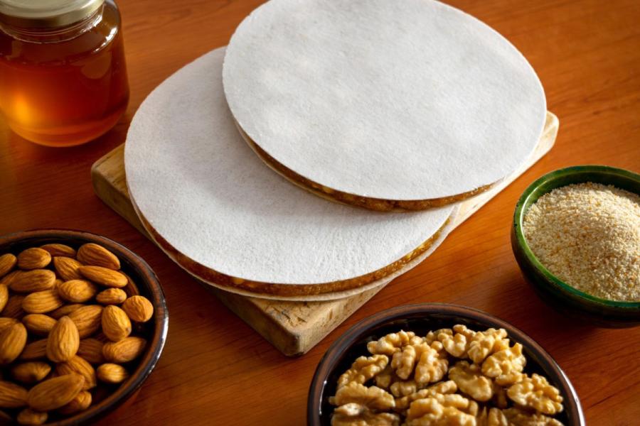 Tortas redondas de alajú cubiertas con oblea, junto a almendras, nueces, miel y pan rallado sobre una mesa de madera.