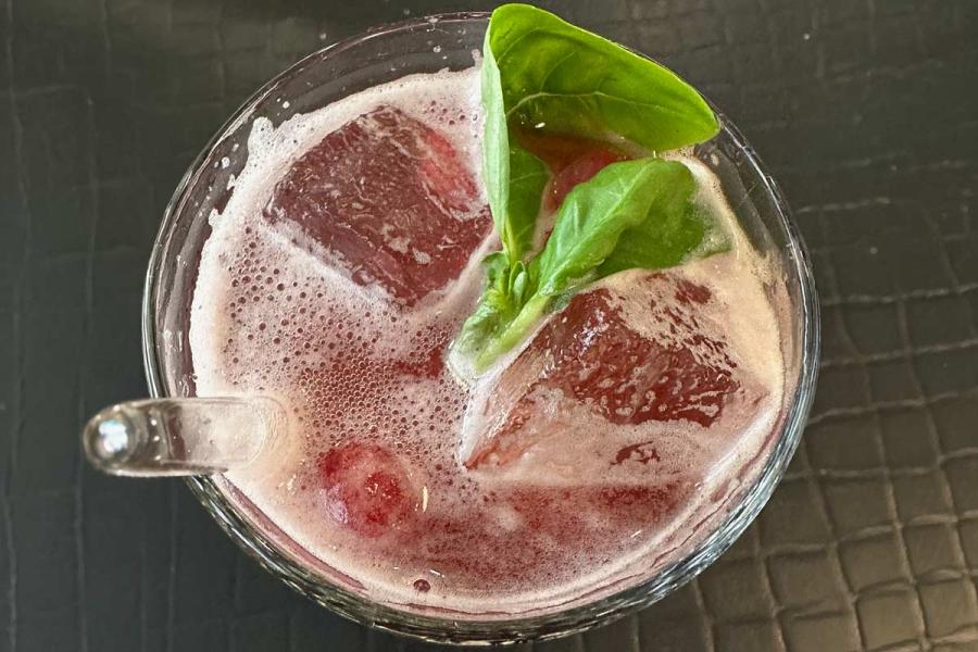 Un vaso con limonada de frambuesa e hibisco alemana, con hielo y hojas de albahaca.