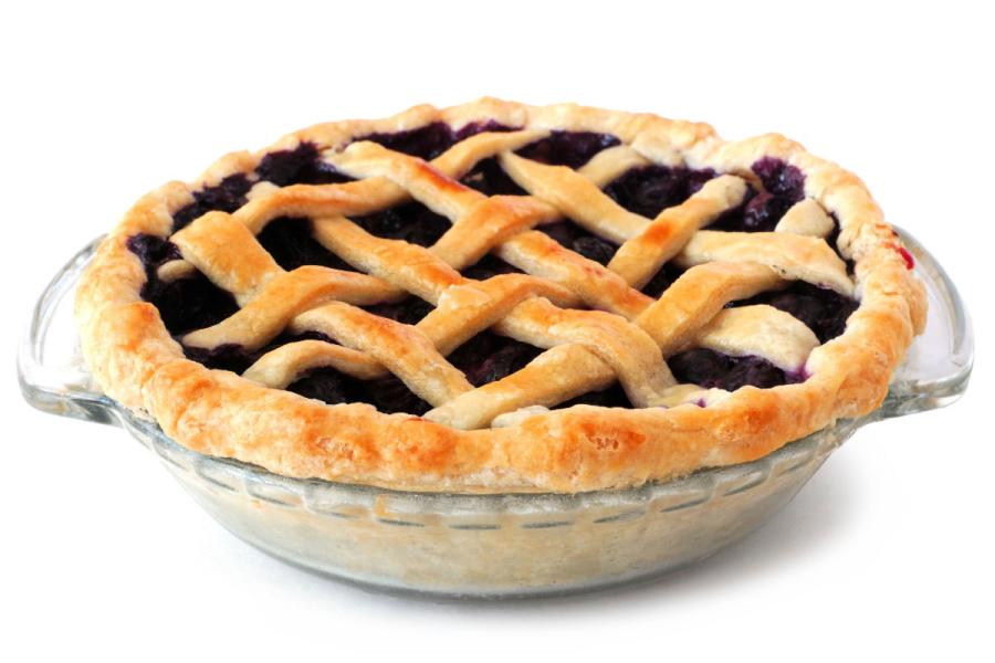 Tarta americana de arándanos azules con cubierta de rejilla de masa dorada, horneada en un molde de vidrio transparente sobre fondo blanco.