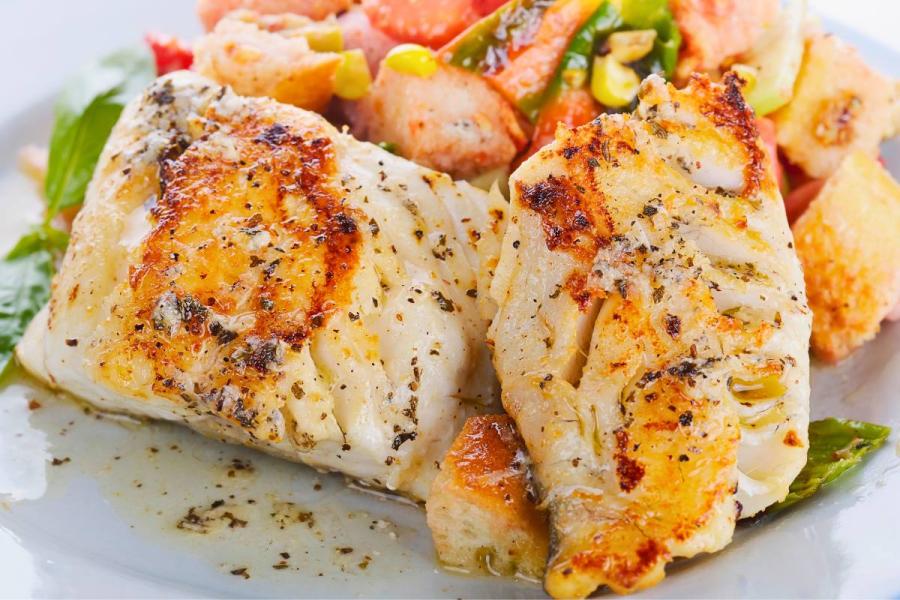 Dos filetes de dorado a la parrilla con hierbas, acompañados de verduras y pan tostado en un plato.