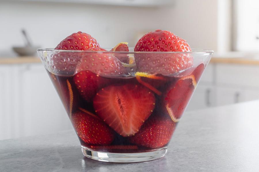 Un recipiente con fresas al vino tinto con piel de naranja finamente cortada.